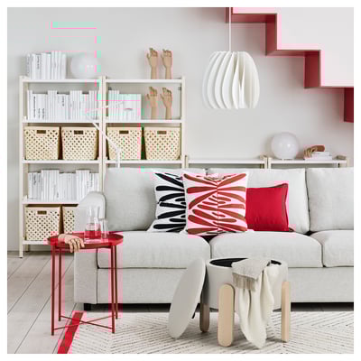 Zona giorno moderna con divano grigio chiaro, cuscini colorati, tavolino in legno e libreria bianca con vari oggetti.