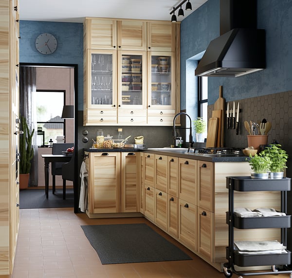 Cucina moderna con armadi in legno chiaro, alzatina in piastrelle esagonali nere ed elettrodomestici in acciaio inossidabile tra cui cappa e fornello.