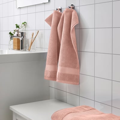 Bagno moderno con asciugamani FREDRIKSJÖN color pesca, appesi e piegati, morbido cotone, fondale piastrellato bianco.