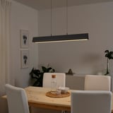 Moderna zona pranzo con lampada a sospensione FRIDSLUND nera su tavolo in legno e sedie bianche.