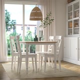 Il tappeto beige si adatta sotto il tavolo da pranzo con 4 sedie, circondato da decorazioni bianche tra cui lampada, vasi e piante vicino alla finestra.