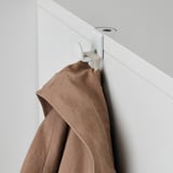 Il cappotto marrone è appeso al gancio da parete bianco, parte del sistema di archiviazione GALANT.