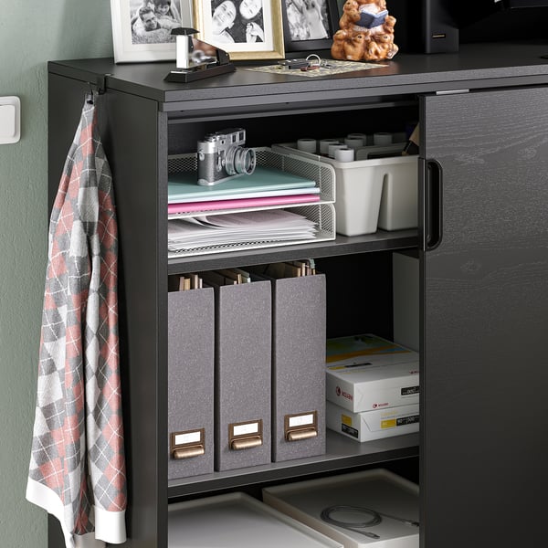 Armadio da ufficio in legno scuro con ripiani regolabili, che contiene file, libri e forniture per ufficio, sormontato da oggetti personali e foto.