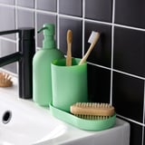 Dispenser di sapone in vetro verde, portaspazzolino e vassoio su lavello bianco. Sfondo della parete piastrellato in bianco e nero.