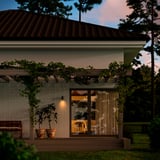 Elegante patio della casa con luci a corda GETKÅL che proiettano una luce calda, vasi di terracotta e panca in legno; Accogliente ambiente notturno.