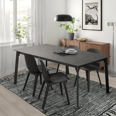 Tavolo da pranzo allungabile con struttura nera, piano in marmo, sedie, ampia finestra, lampada, credenza, pianta.