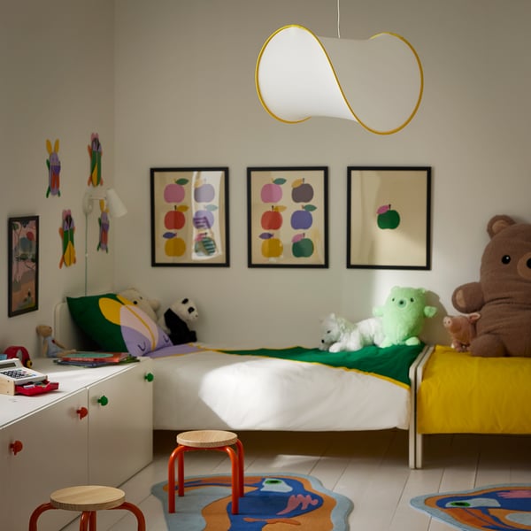 Cameretta per bambini con letto bianco, tappeti colorati, peluche e una moderna lampada da soffitto con un design giocoso e aperto che fornisce una luce soffusa.
