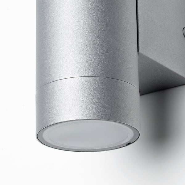 Moderna lampada da parete cilindrica, caratterizzata da un'elegante finitura in acciaio inox, è progettata per uso esterno.