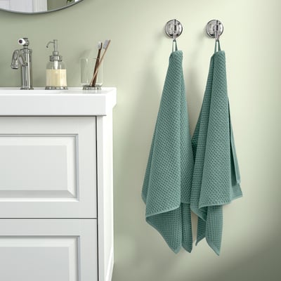 Bagno verde salvia con lavandino cromato, asciugamani e spazzolini da denti.