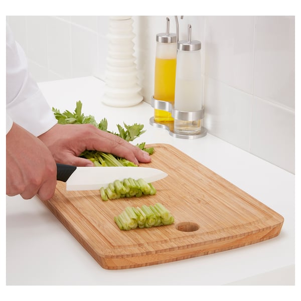 Persona che taglia il sedano sul tagliere di bambù con coltello in ceramica affilato.