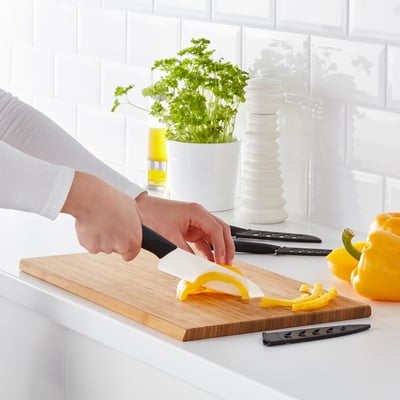 La persona affetta il peperone giallo sul tagliere di legno usando un coltello in ceramica. Il set HACKIG comprende vari coltelli, affilati e resistenti.