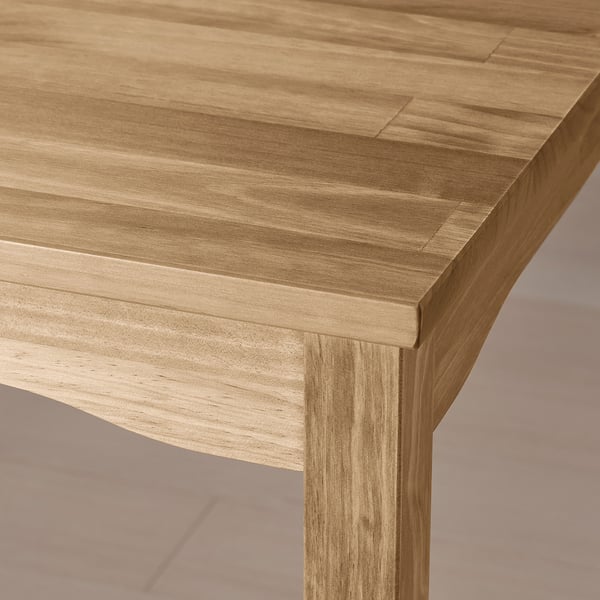 Un primo piano di un tavolo da pranzo in legno chiaro che mostra la sua finitura liscia e naturale e la forte falegnameria.