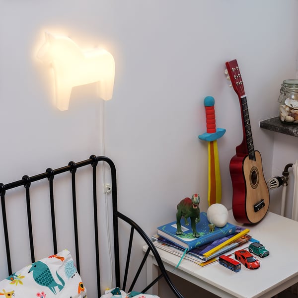 Lampada da comodino a forma di testa di cavallo che illumina la cameretta di un bambino con giocattoli e libri su un comodino.
