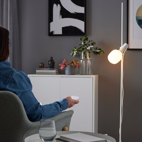 Persona seduta sulla sedia, che tiene il telecomando, controllando la moderna lampada da terra con dimmerazione wireless e cambio colore.