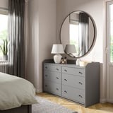 Una camera da letto moderna con un'ampia cassapanca HAUGA grigia, specchio rotondo e lampade bianche.