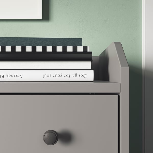 Una cassettiera HAUGA grigia con un libro bianco intitolato design for your soul sulla parte superiore. Linee eleganti, manopole rotonde e design moderno.