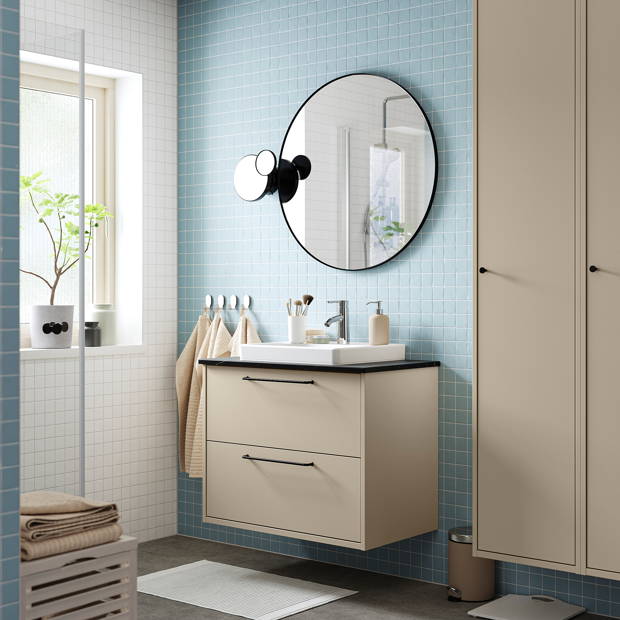 Bagno moderno con mobile HAVBÄCK beige, piastrelle azzurre, lavandino quadrato bianco, specchio rotondo, applique.