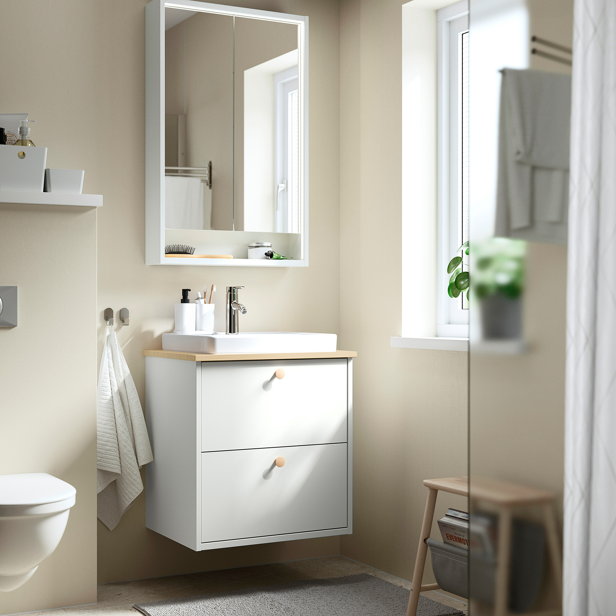 Moderno mobile da bagno a parete in bianco con bancone in legno chiaro, specchio, due cassetti, lavandino in argento, asciugamano appeso e piccola pianta.