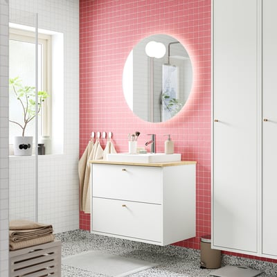 Moderno mobile da bagno bianco, specchio rotondo, piano di lavoro in bambù, piastrelle rosa. Asciugamani su rastrelliera.