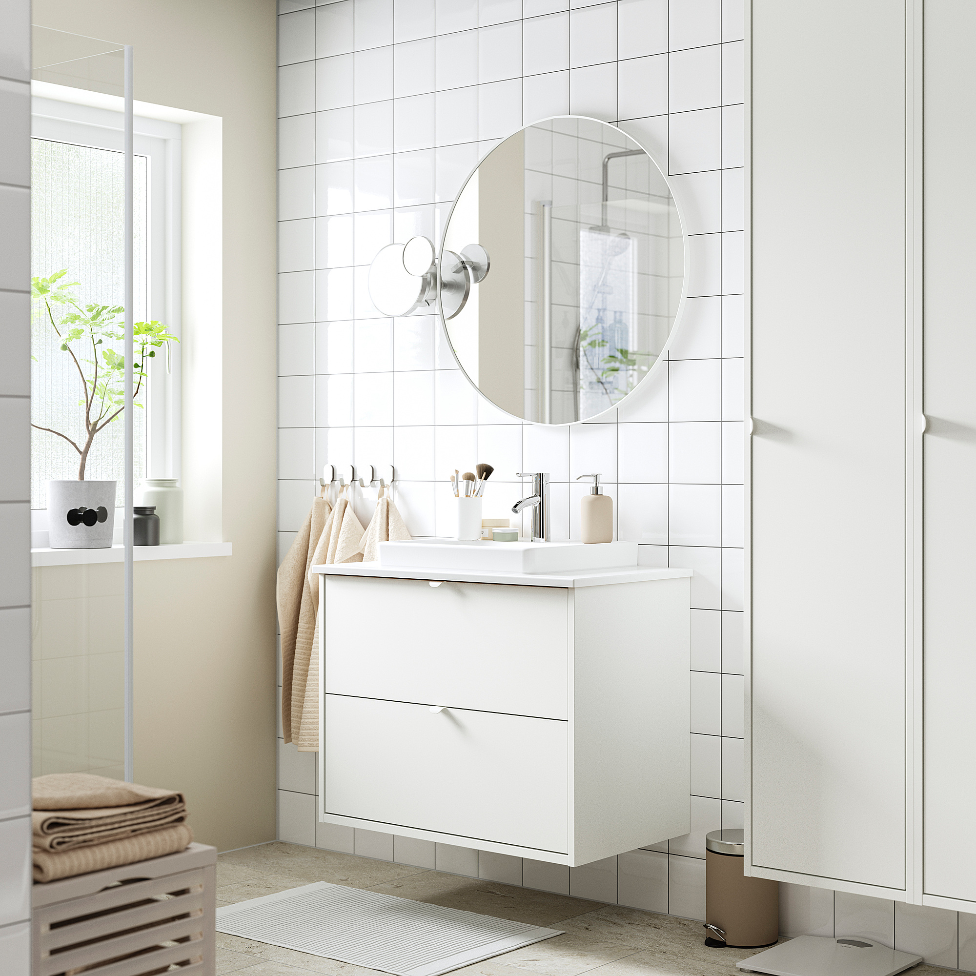 Bagno bianco minimalista con lavabo HAVBÄCK, specchio rotondo, tappeto beige, pianta e asciugamani.