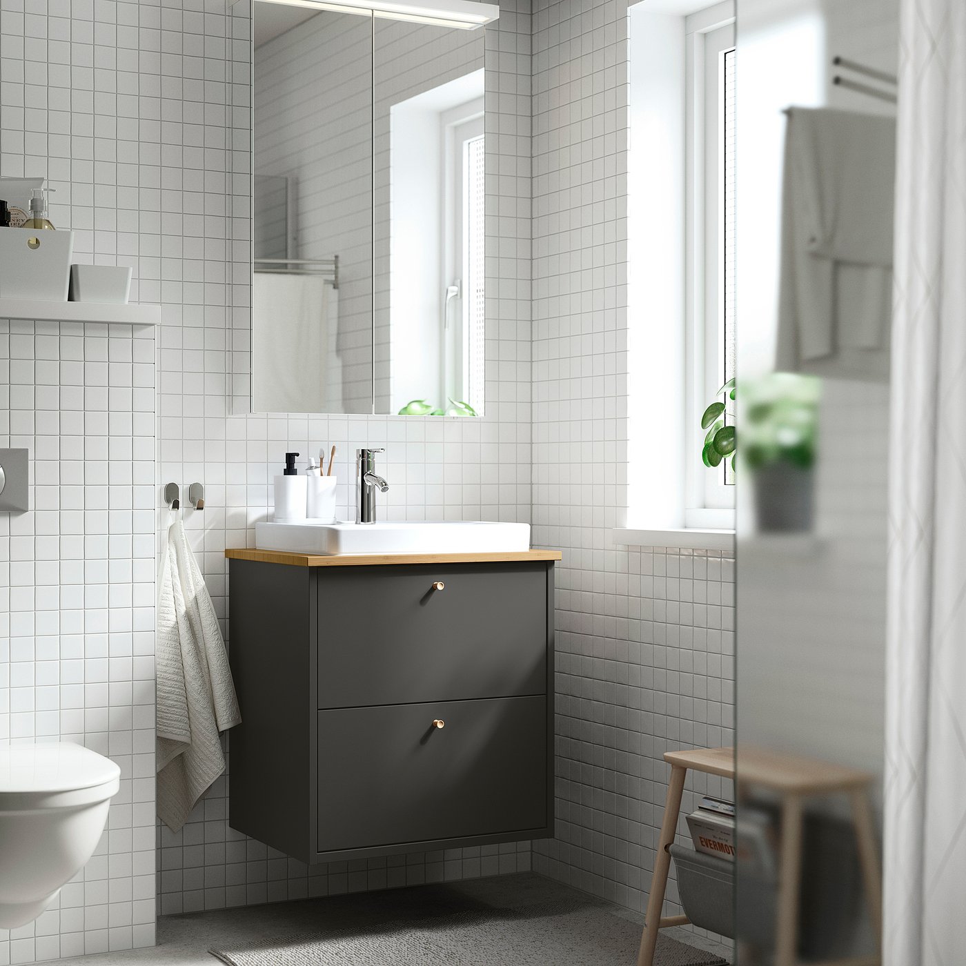 Bagno moderno con lavabo ikea grigio, lavandino bianco, bancone in legno, specchio, sgabello, asciugamani, pianta, minimalista.