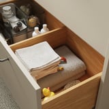 Cassetto aperto che mostra asciugamani ben piegati e paperelle di gomma. Soluzione di archiviazione del bagno con contenitore chiuso e finitura in legno.