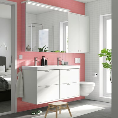 Bagno moderno con doppio lavabo bianco, due lavandini, piastrelle rosa, grande specchio, sgabello in legno e finestra.