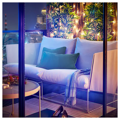 Un balcone moderno con divano HAVSTEN, cuscini, plaid e fiori.