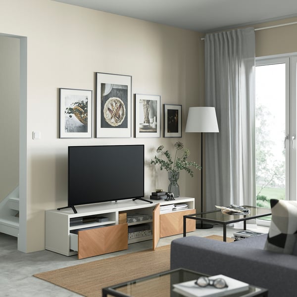 Soggiorno moderno con tv su supporto in rovere, quadri incorniciati e tavolino in vetro di fronte al divano grigio.