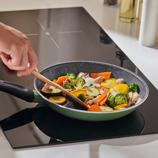 Una persona cucina un soffritto colorato in una padella antiaderente verde su un piano cottura a induzione.
