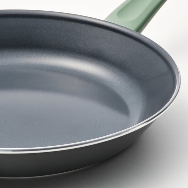 Padella antiaderente grigia con manico verde su superficie bianca, che mostra una superficie liscia e uniforme e un manico robusto.