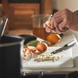 Persona che spreme il limone su aglio, cipolle e verdure sul tagliere bianco in cucina.