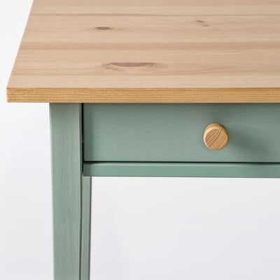 Un tavolino HEMNES in legno grigio-verde con piano in legno chiaro. Ha un cassetto e un ripiano, che offrono sia spazio che esposizione.