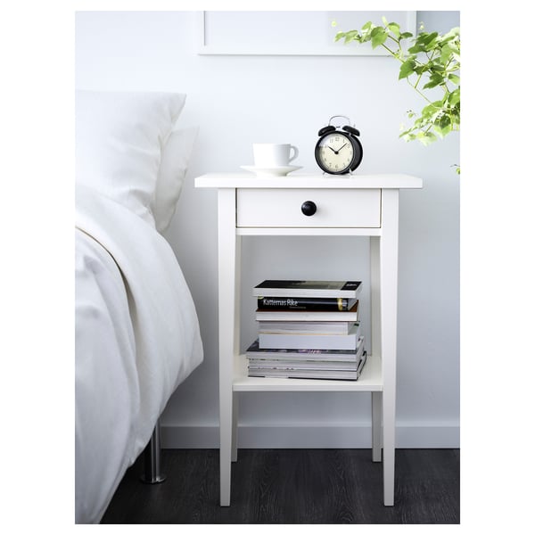 Comodino HEMNES bianco con orologio nero, tazza da caffè, libri. Design alto, snello, in legno. Si adatta perfettamente accanto al grande letto.