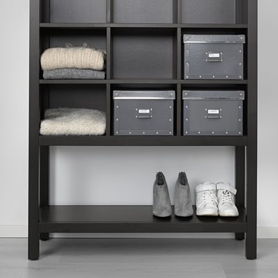 Scaffale in legno nero con scarpiera e vestiti piegati. Le scatole organizzano gli accessori.