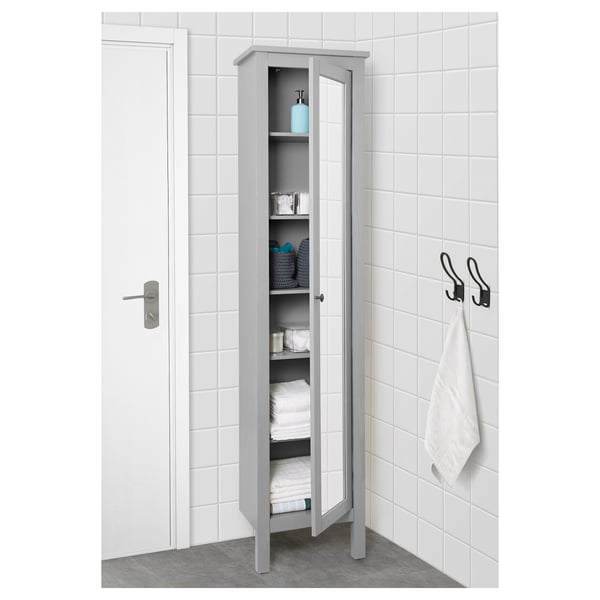 Un alto armadietto grigio con una porta a specchio piegato ordinatamente, asciugamani e forniture per il bagno. Quattro ripiani regolabili offrono ampio spazio di archiviazione.
