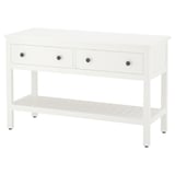 Una consolle HEMNES bianca. Ha tre cassetti con pomelli in argento e un ripiano aperto. Il design è semplice e funzionale.