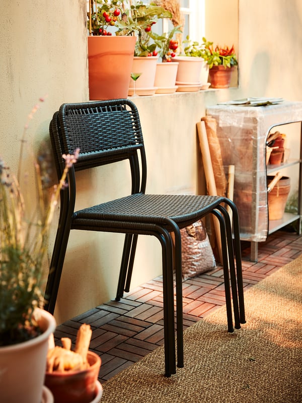 Sedia in vimini nero su patio piastrellato con piante in vaso, creando accoglienti posti a sedere all'aperto.