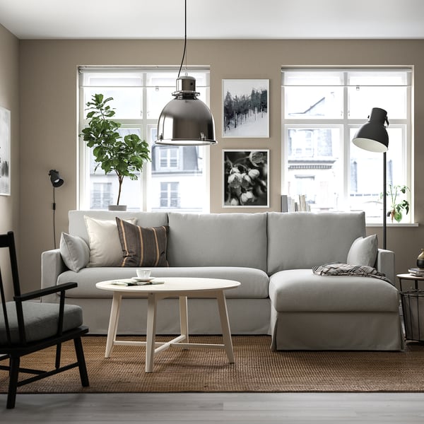 Soggiorno moderno con divano componibile HYLTARP grigio chiaro, ampi cuscini, tavolino rotondo e lampada a sospensione. Le ampie finestre forniscono luce naturale.