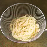 Schiumatoio in acciaio inox riempito con tagliatelle cotte, ideale per filtrare.