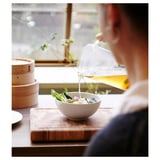 Versare il liquido giallo sull'insalata in una ciotola bianca vicino alla vaporiera di bambù.