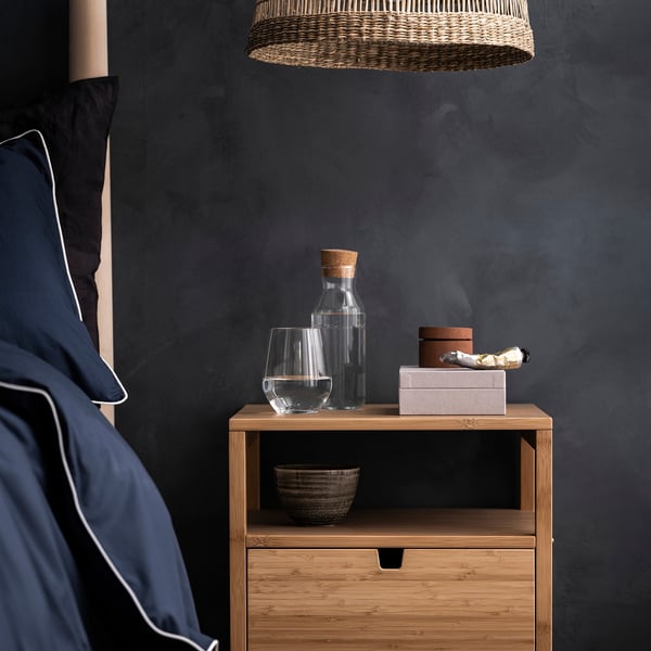 Comodino moderno con caraffa in vetro, bicchiere da vino, scatole e ciotola. Caraffa con coperchio in sughero, ripiani aperti in legno.