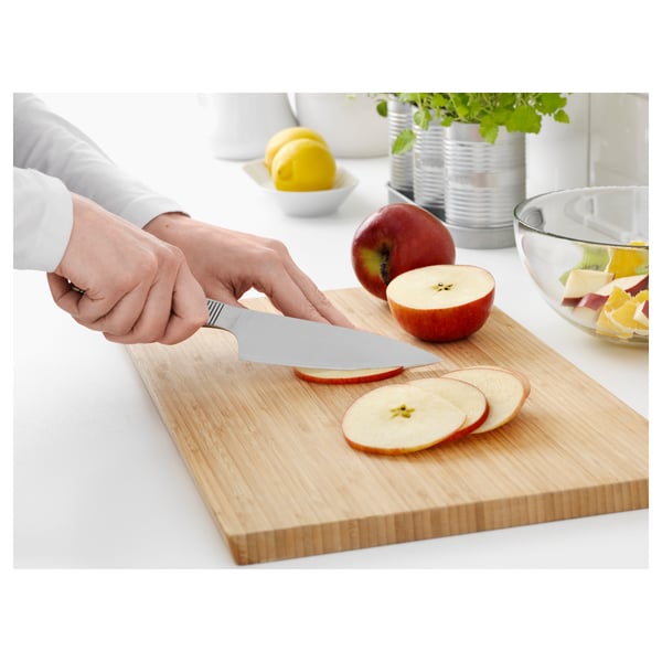Mani che affettano la mela sul tagliere di legno del coltello ikea, coltello inossidabile, ciotola di frutta nelle vicinanze.