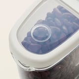 Barattolo trasparente con coperchio bianco, che mostra le caramelle viola conservate. Design trasparente per una facile visualizzazione.