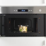 Forno a microonde da incasso con contenitore in vetro per scaldare gli gnocchi, con timer digitale sul pannello di controllo.