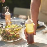 Mano che tiene la bottiglia gialla IKEA 365+ con etichetta condimento per insalata sopra la ciotola di insalata.