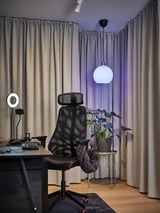 Home office nero con scrivania, lampada, sedia, luce ad anello, pianta, tende grigie.