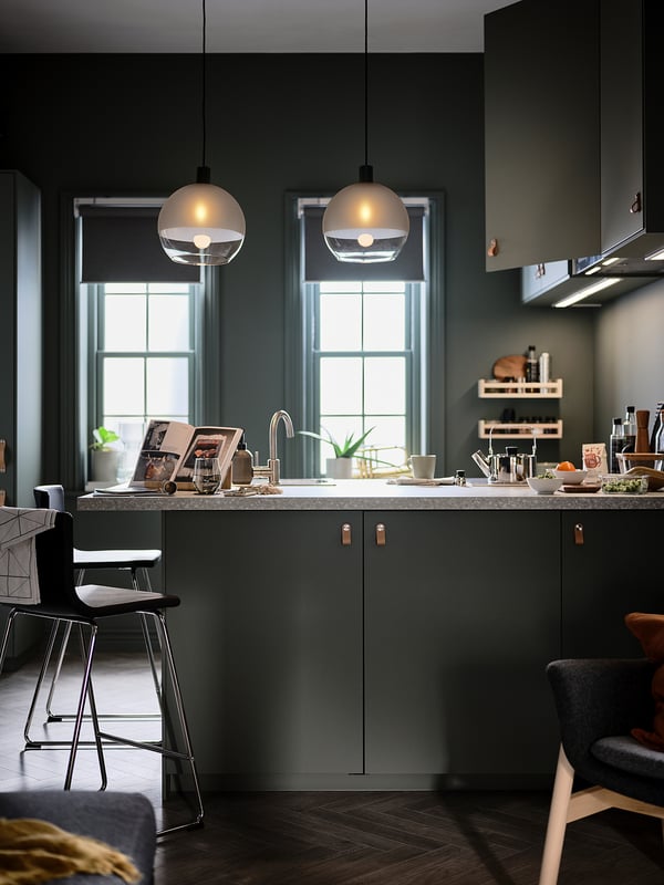 Cucina moderna con armadi verde scuro, due lampade a sospensione sferiche e piano di lavoro grigio chiaro.