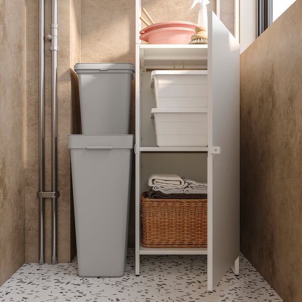 Armadio pulito con ripiani bianchi, bidoni grigi, cesto di vimini e oggetti rosa.