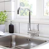 Lavello da cucina moderno con rubinetto cromato, distributore di sapone nero e pianta verde.